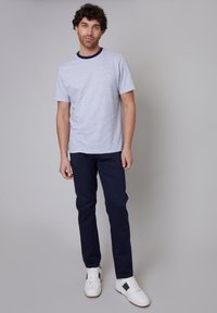 T-shirt à rayures à manches courtes avec un col côtelé bleu marine, associée à un pantalon bleu marine et des baskets blanches avec des accents noirs.