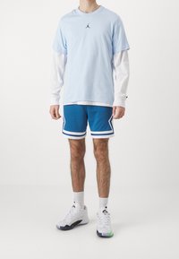 Vaaleansininen t-paita valkoisen pitkähihaisen paidan päällä, siniset verkkoshortsit valkoisilla raidoilla, ja valkoiset koripallokengät.