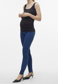 Svart, åtsittande linne, blå smala jeans och svarta slingback-hälar. Klädseln betonar en mjuk, avslappnad design med slim fit.