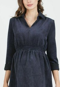 Marineblaues Cord-Kleid mit Kragen, dreiviertellangen Ärmeln und gerafftem Taillenbereich, das eine weiche Textur und ein geripptes Muster aufweist.