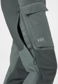 Vodotěsné venkovní kalhoty v tmavě šedé barvě, s cargo kapsou, bočním zipem a texturovanou tkaninou pro odolnost a výkon.