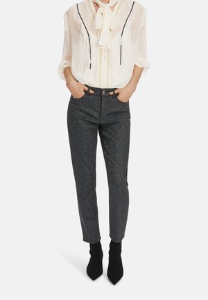 Grau Denim-Hosen mit schwarzem Leopardenmuster, hoher Taille, Fronttaschen und einzigartigem Hardware-Detail an der Taille. Kombiniert mit einem cremefarbenen Oberteil.