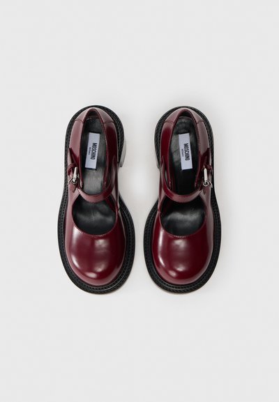 Chaussures en cuir bordeaux avec un bout arrondi, un design découpé, une sangle ajustable et une semelle noire texturée. Détails en métal argenté inclus.