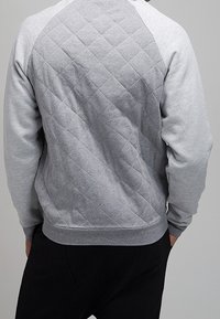 Szary pikowany sweatshirt z diamentową teksturą na plecach i kontrastowymi, jednolitymi szarymi rękawami, z żebrowanym dołem i mankietami.