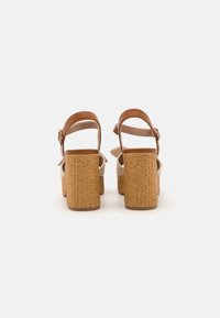 Beige platform sandals with a woven texture and brown ankle straps. Features block heels for stability and a smooth surface.