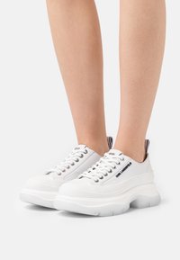 Baskets à plateforme blanches avec une tige en cuir lisse. Dotées d'œillets métalliques, d'une semelle épaisse et d'un détail de logo sur le côté et la languette du talon.