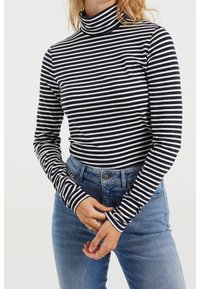 Svart och vitrandig långärmad turtleneck-top med åtsittande design, mjukt tyg, hög krage och kontrasterande randiga manschetter. Blå denimjeans.