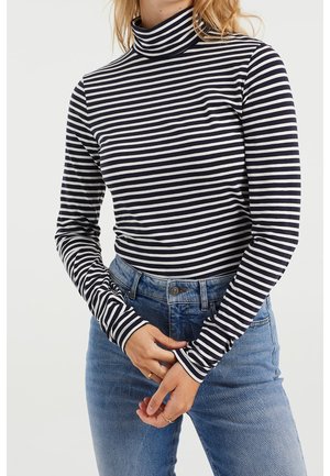 Sort-hvid stribet langærmet turtleneck-top, tætsiddende design, blødt stof, med høj krave og kontrasterende stribede manchetter. Blå denim jeans.
