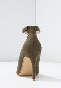 Zelená semišová lodička na vysokém podpatku se strapcem. Vyznačuje se špičatou špičkou a úzkým jehlovým podpatkem. Hladká textura s minimalistickým designem.