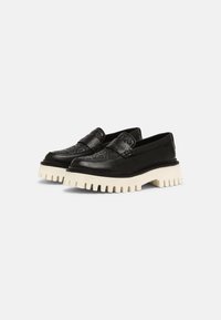 Mocassins en cuir noir avec un dessus texturé et de épaisses semelles crantées blanches, présentés côte à côte sur un fond clair et uni.