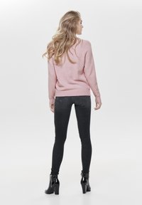 Rosa, weicher Pullover mit langen Ärmeln; kombiniert mit schwarzen, eng anliegenden Jeans und schwarzen High Heels. Einfaches Design ohne Muster.