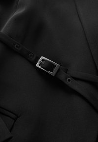 Black fabric features a smooth texture, with a matte finish, complemented by a silver metal buckle and black straps attached by buttons.
