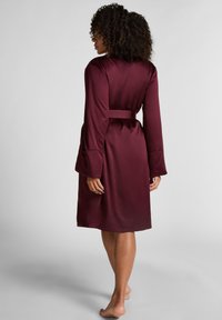 Burgunderfärgad satinroben med långa utställda ärmar, midjeband och slät textur, visad bakifrån mot en ljus bakgrund.