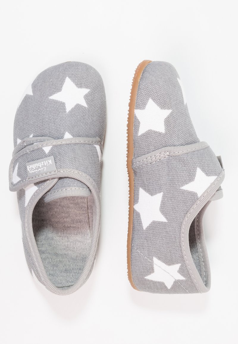 Pantofole in tessuto grigio con motivi bianchi a stelle, dotate di una fascia in velcro e suola in gomma marrone. Texture morbida con forma arrotondata.