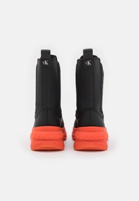Czarne wysokie botki z teksturowanym wykończeniem, kontrastową pomarańczową gumową podeszwą oraz uchwytami z logo na pięcie.