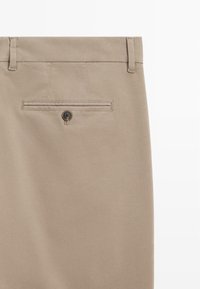 Beige Hosen aus einem glatten Stoff mit Gürtelschlaufen, einer hinteren Tasche mit Knopfverschluss und subtilen Nähdetails.