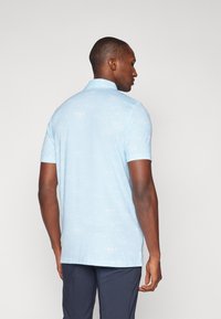 Hellblaues Poloshirt aus glattem Stoff, mit einem dezenten geprägten Muster mit Naturmotiven. Kurze Ärmel und klassischer Kragen.