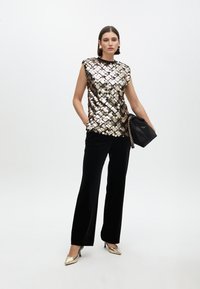 Sequin top with round neck and sleeveless design in gold, silver, and black; paired with black velvet trousers and metallic heels. Black bag accent.