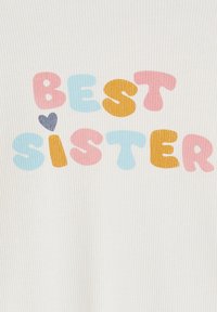 "Colorful playful text 'BEST SISTER' with a small heart above the letter 'I' on a ribbed white fabric background."