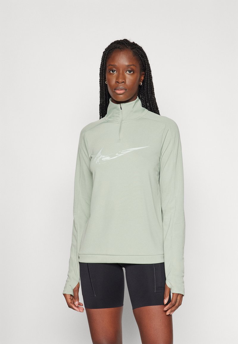 Top de manga larga verde menta con cuello alto y cremallera de cuarto. Presenta un logo blanco en el pecho y un corte ajustado. Se lleva con pantalones cortos negros.