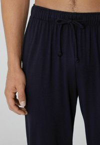Navyblauwe loungebroeken van zachte stof, met een elastische tailleband en een trekkoord. Hand zichtbaar aan de linkerkant.