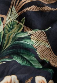 Sötét szövet zöld levelekből és bézs botanikai mintákból álló nyomattal, redőkkel és textúrával.