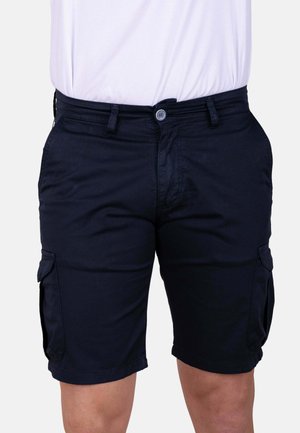 Hombre con pantalones cortos cargo negros con bolsillos laterales y una camisa blanca metida por dentro, mostrado desde la cintura hasta la mitad del muslo.