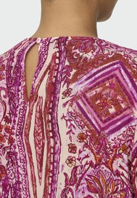 Multicolored blouse featuring pink, burgundy, and cream floral paisley patterns. Keyhole back closure with a small button accent. Soft fabric texture.