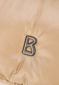 Un tessuto imbottito beige con una texture liscia presenta una prominente lettera nera "B" come accento. Il design è morbido e accogliente.