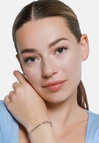 Bracciale in argento con maglie allungate, indossato su un polso di pelle chiara; la persona ha i capelli lisci e indossa una maglietta azzurro chiaro.