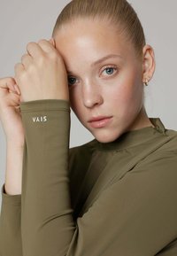 Olijfgroene, lange mouw top van gladde, rekbare stof, met een hoge halslijn en een wit logo op de manchette.