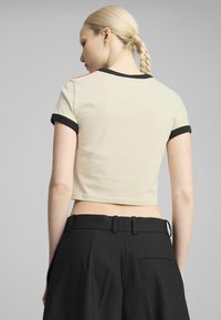 Beschnitten beige t-shirt med sort kant og orange detaljer, parret med højtaljede sorte bukser. Glat bomuldsstof.