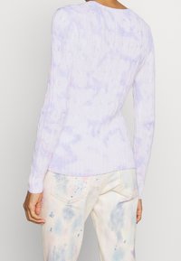 Sweter z dzianiny w jasnofioletowym kolorze z wzorem tie-dye, z prążkowanymi mankietami i dołem. Połącz z pastelowymi spodniami w wzór rozchlapania farby.