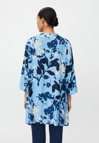 Kwiecista tunika w jasnoniebieskim kolorze, zdobiona granatowo-białymi wzorami botanicznymi. Luźny krój z rękawami do pół łokcia i okrągłym dekoltem.