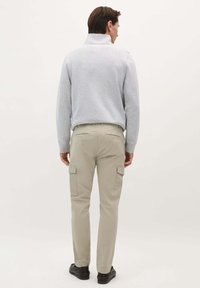 Pulover din fleece gri deschis cu guler înalt, purtat cu pantaloni cargo bej, cu buzunare laterale și o croială slim. Pantofi negri completează ținuta.