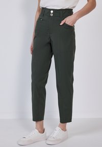 Pantaloni verdi con vita alta, dotati di chiusura a bottone, tasche laterali e gamba affusolata. Tessuto in misto cotone e texture liscia.