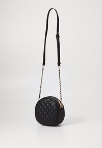 Borsa a tracolla in pelle nera trapuntata, di forma circolare, con hardware dorato e una tracolla a catena removibile. Chiusura con zip sulla parte superiore.