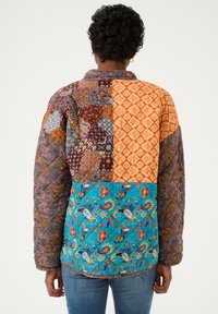 Jachetă patchwork cu diverse modele în nuanțe de portocaliu, albastru, maro și mov. Material texturat, cu guler și mâneci lungi.