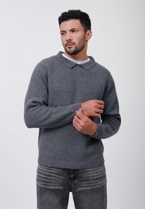 Grijze geribde trui met kraag, voorzien van lange mouwen en een relaxte pasvorm. De textuur is dik gebreid, gecombineerd met donkergrijze spijkerbroeken.