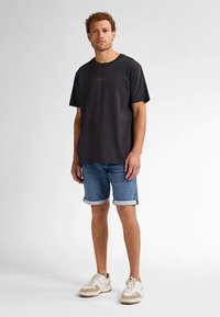 Zwart T-shirt met korte mouwen en een ronde hals, gecombineerd met blauwe denim shorts met omgeslagen zoom en beige sneakers met accenten.