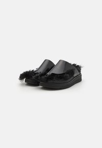 Svarta glidskor med en glänsande plastöverdel och en fluffig trim längs kanten. Platt sula med en strukturerad svart gummibotten.
