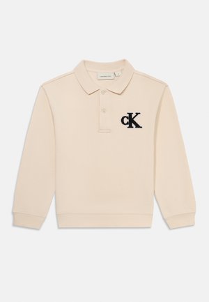 Beige pikkade varrukatega polo särk kraega, mille vasakul rinnal on sinise värviga tikitud "ck" logo, valmistatud tekstureeritud kangast.