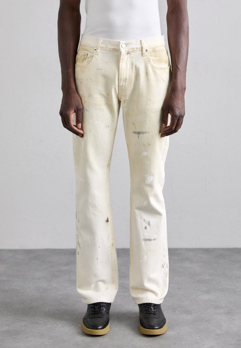 Jean en denim blanc avec des tâches usées, un design droit et un style à cinq poches. Portez avec des chaussures noires et un débardeur blanc ajusté.