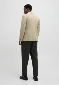 Beige blazer with a tailored fit, single back vent, and button accents, paired with dark gray trousers and black shoes.