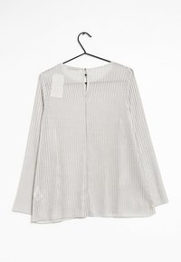 Lichtgrijze, lange mouwen top met een geribbeld textuur, ritssluiting aan de achterkant en zijsplitten aan de onderrand. Hangt aan een zwarte haak.