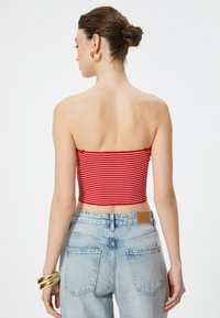 Top corto a righe rosse e bianche abbinato a jeans in denim azzurro a vita alta. Bracciale d'oro al polso, design semplice, senza chiusure visibili.