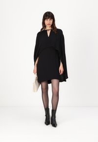 Črna obleka s plaščem. Ima dekolte v obliki ključavnice, kratko dolžino in gladko tkanino. Ujemajo se z antilop čevlji in kremasto torbico.