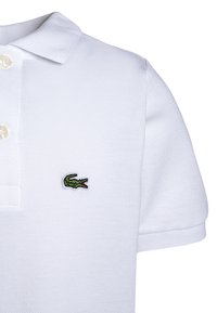 Polo shirt bianco realizzato in tessuto testurizzato con una patta a tre bottoni. Presenta un piccolo logo di coccodrillo verde sul petto.