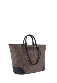 Ruskea tilkkukangaskassi mustilla nahkaosilla, joissa on kaksoiskahvat ja kohopainettu kukkakuosi. Sivussa on brändin logo.