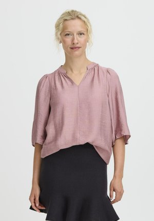 Rosa Bluse mit kurzen Ärmeln und V-Ausschnitt, texturiertem Stoff und Raffung am Kragen, kombiniert mit einem schwarzen, figurbetonten Rock.